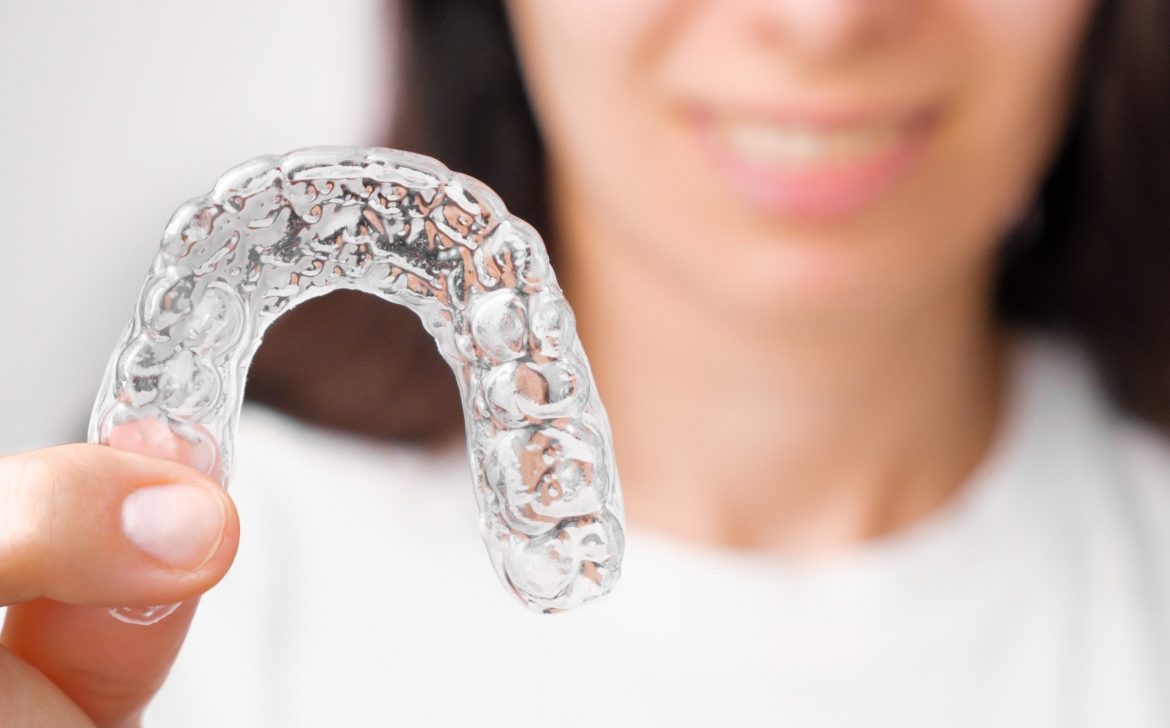 Close up orthodontic transparent aligner in womans hand. Removable braces.
